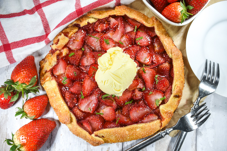 Horizontal shot of a galette with fresh berries, forks, a tea towel, and a scoop of ice cream