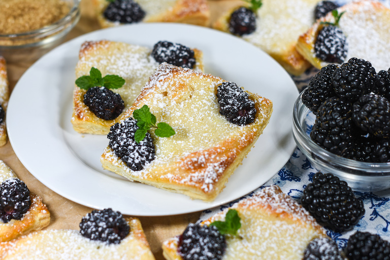 A pair of blackberry pastries on a white plate with dish of fresh berries
