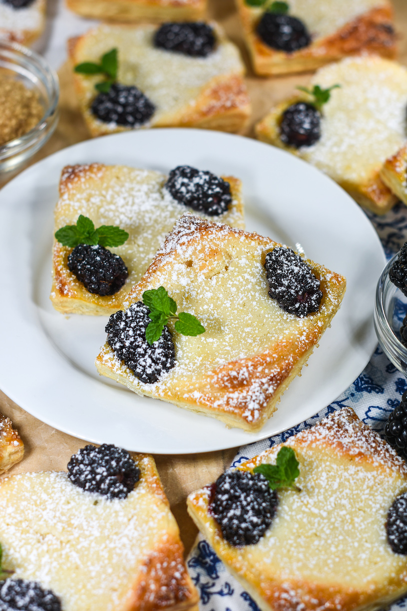 A white plate with a pair of square shaped blackberry puff pastries with goat cheese
