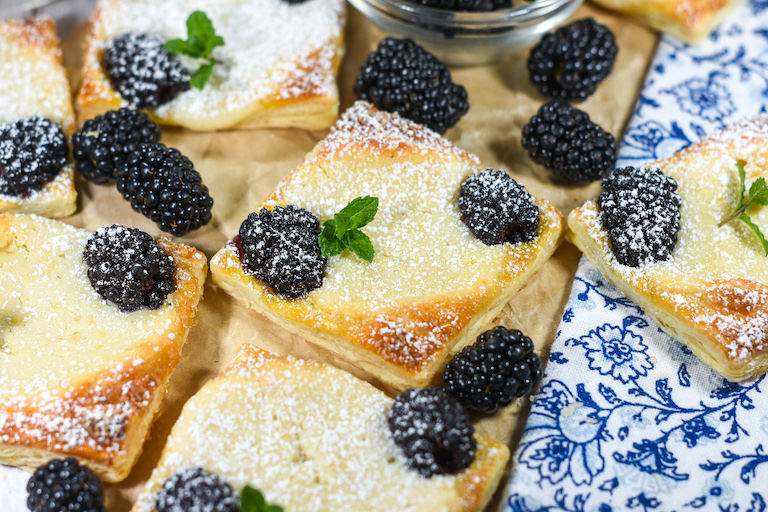 Blackberry puff pastry squares and fresh blackberries with a blue floral tea towel