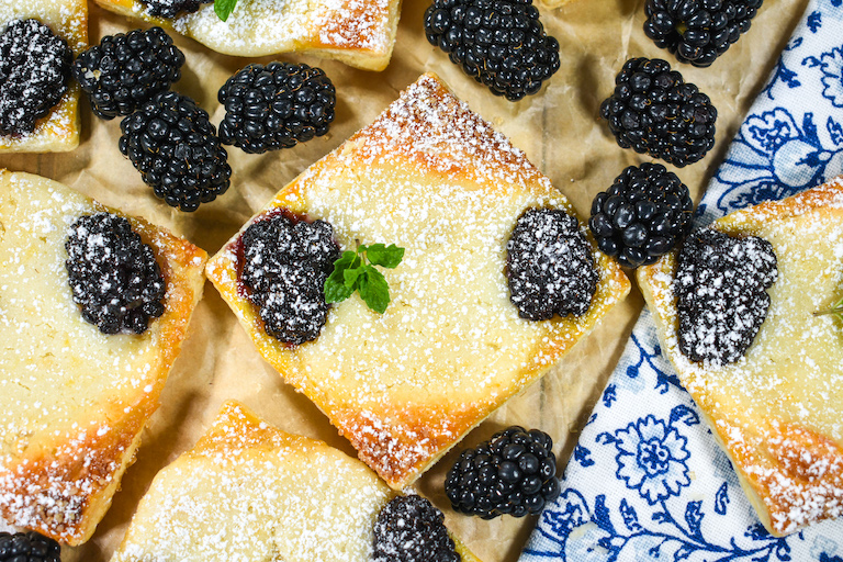 Square shaped blackberry cheese pastries with a blue tea towel