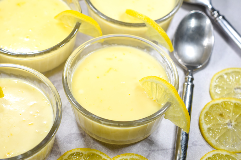 Lemon posset in a dish with a wedge of lemon on the rim, and a metal spoon