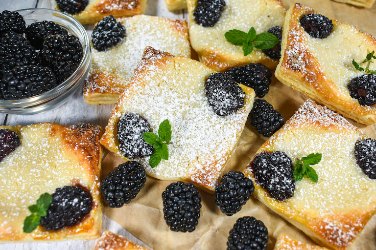 Blackberry pastries and a dish of ripe berries on a sheet of baking parchment
