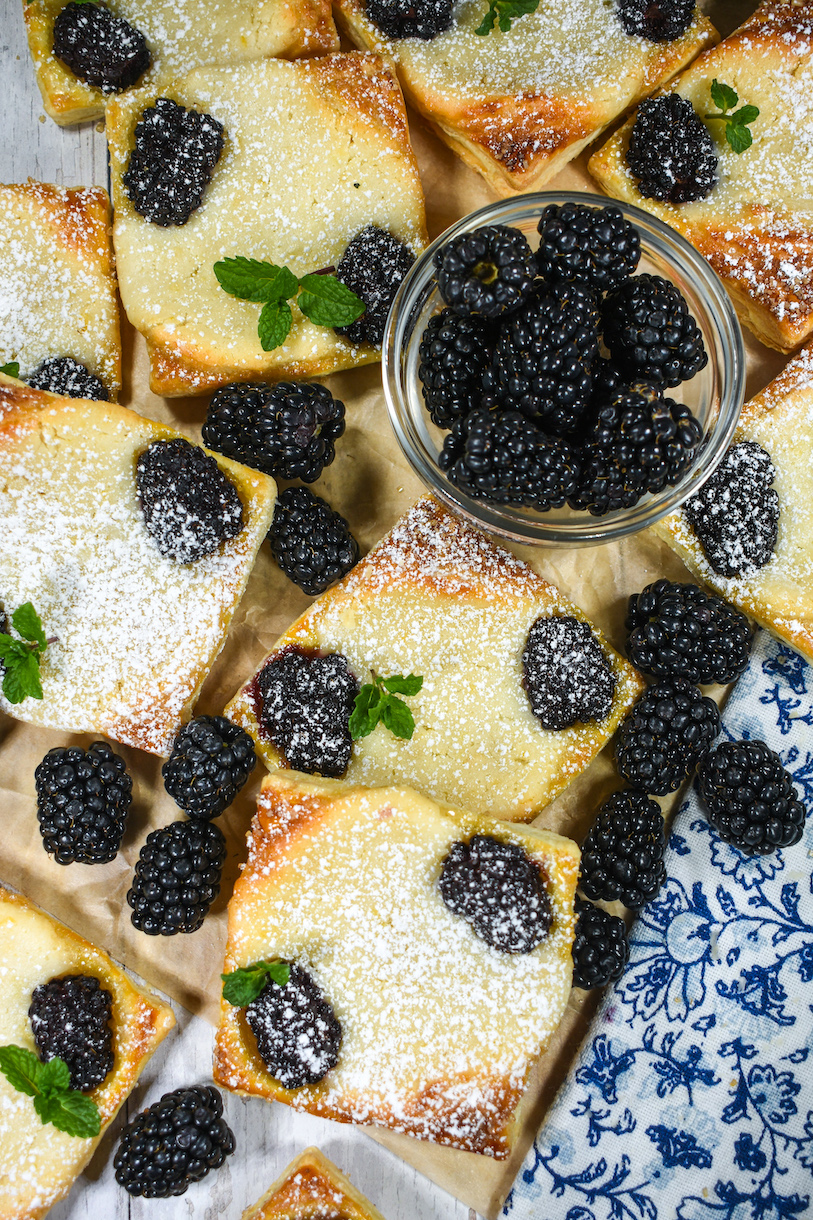 A dish of blackberries and squares of puff pastry with cream cheese and berries, dusted in powdered sugar
