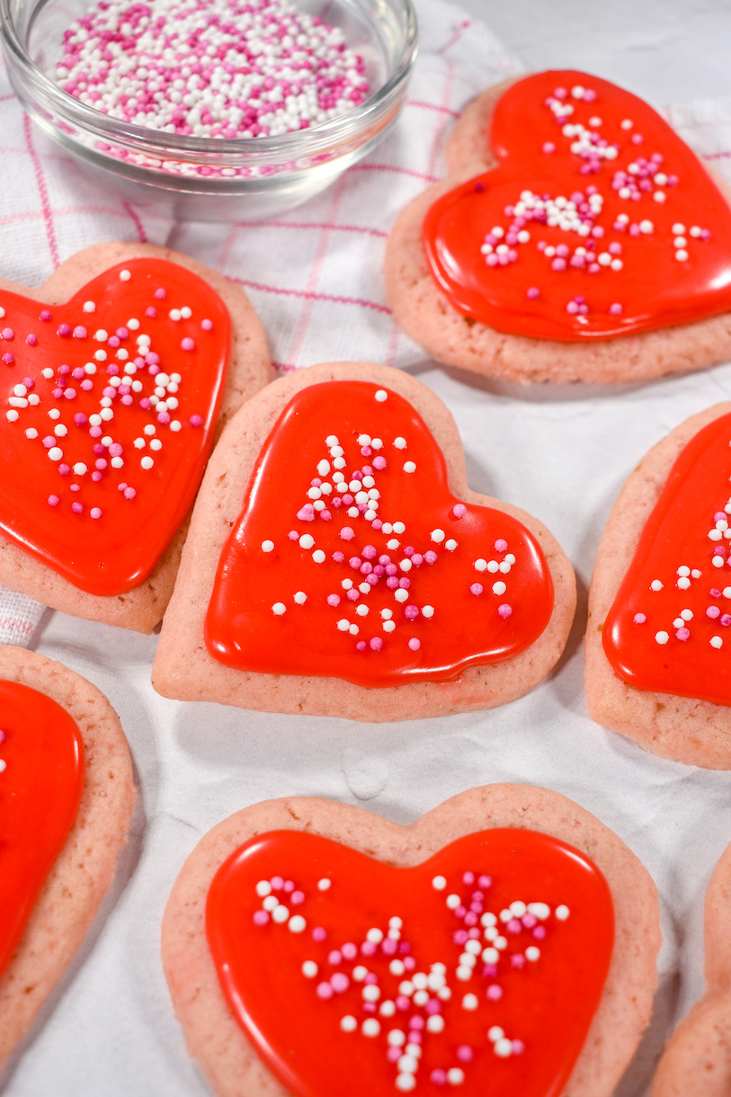 Heart cookies on a white surface with towel and bowl of sprinkles