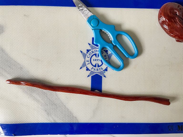 A rope of hot sugar and a pair of kitchen shears on a silicone mat