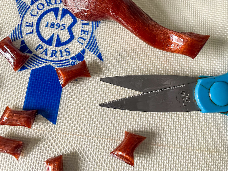 A pair of scissors and pieces of homemade hard candy on a silicone mat