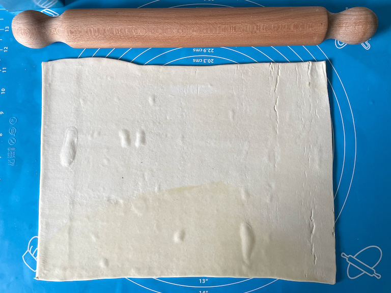 Rolling pin and sheet of puff pastry on blue mat

