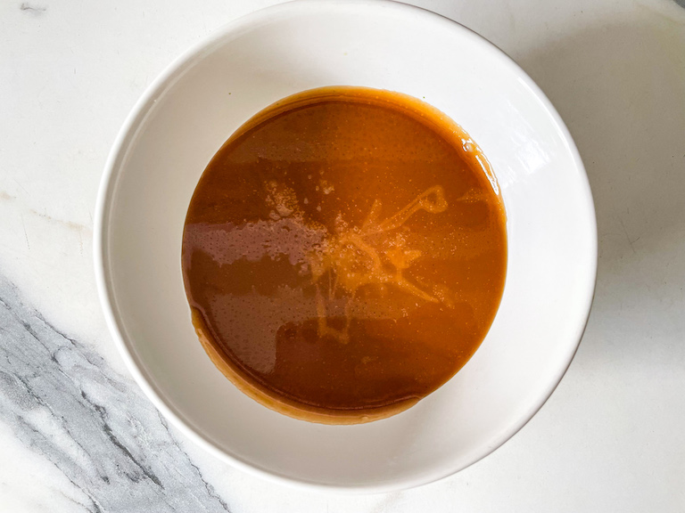 A bowl of caramel sauce on a marble countertop