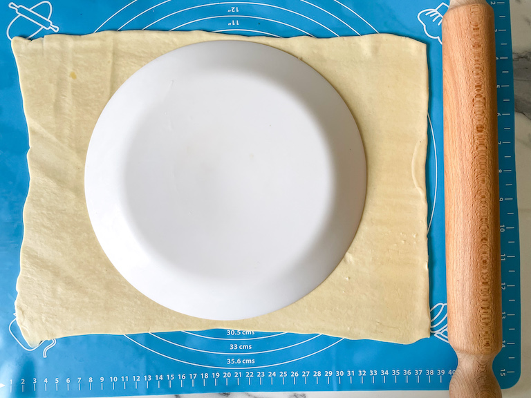 Sheet of pastry on a rolling mat with a plate, along with a rolling pin