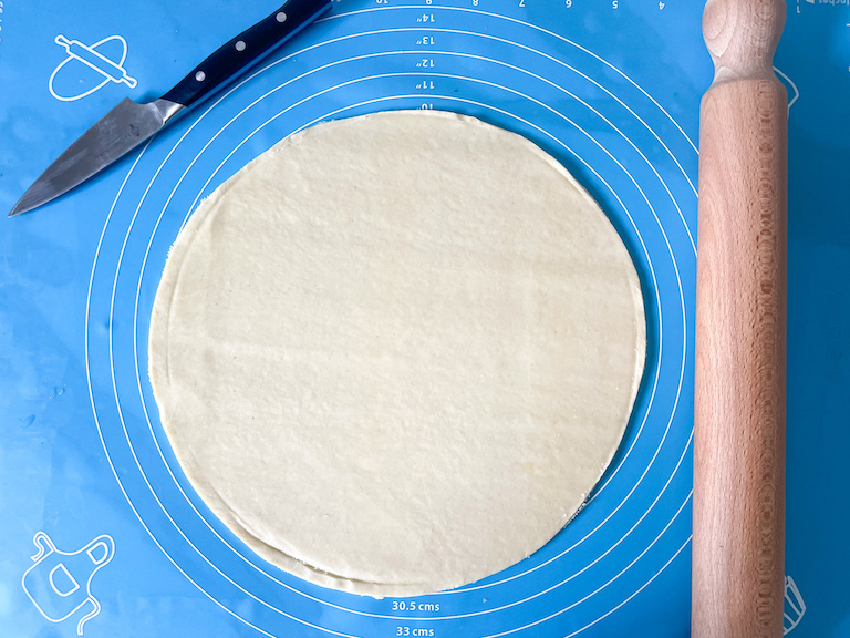 Disc of shortcrust pastry on a rolling mat with a knife and rolling pin