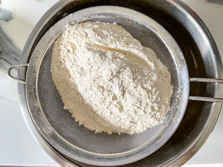 Sieve of flour above a metal bowl