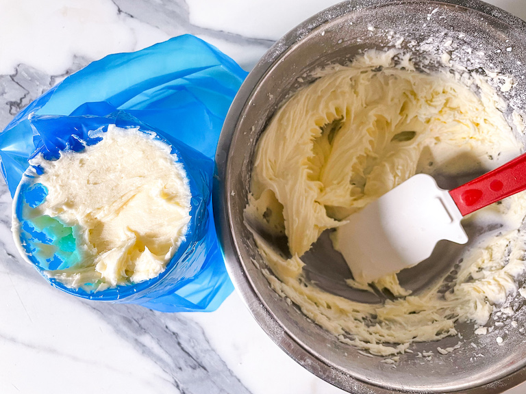 A piping bag of cream filling and a bowl of filling with a rubber spatula, arranged on a marble countertop