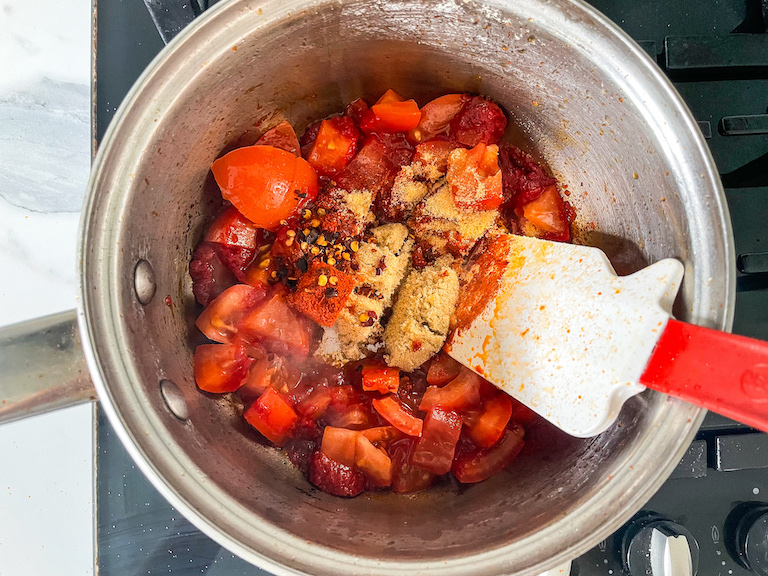 Tomatoes and spices in a saucepan with a spatula