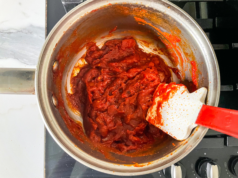 Saucepan on stovetop with tomato jam and a spatula