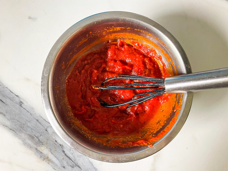 Tomato jam in a small metal bowl with a whisk