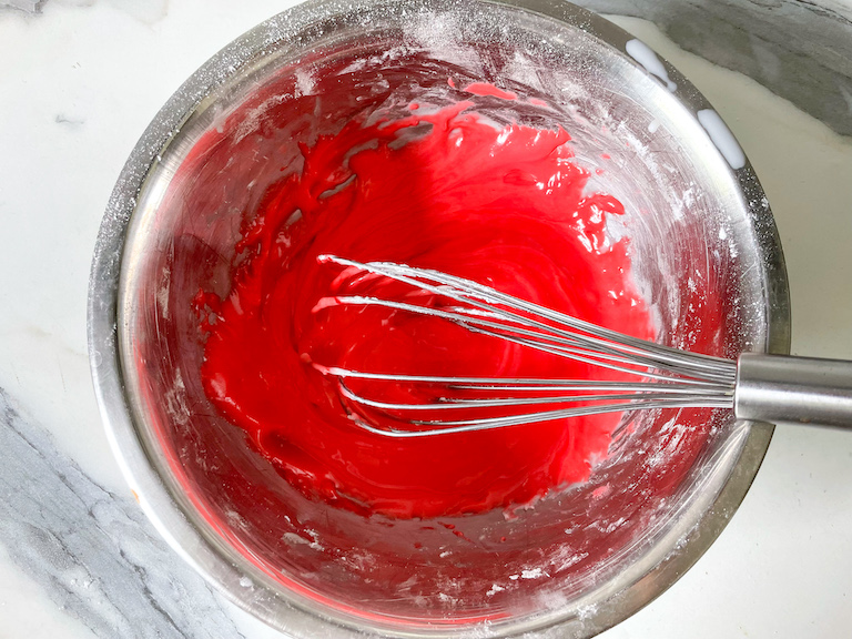 Red icing in a bowl with a whisk