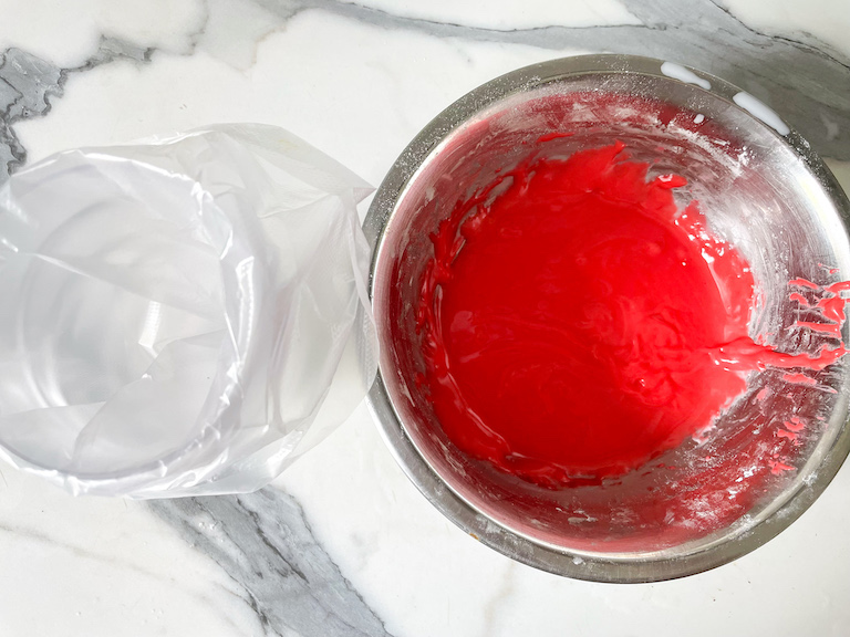Metal bowl with red icing and a piping bag