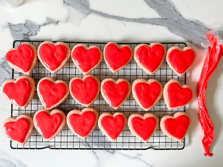 Heart cookies with red icing arranged on a wire rack