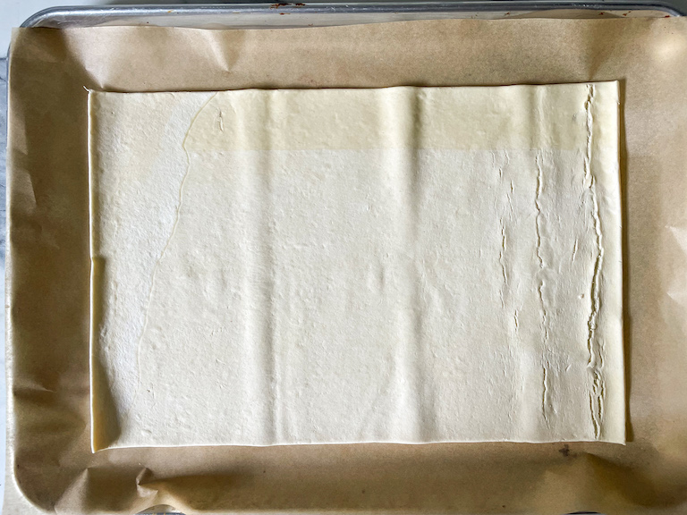 A rectangle of unbaked puff pastry unrolled on a parchment lined tray