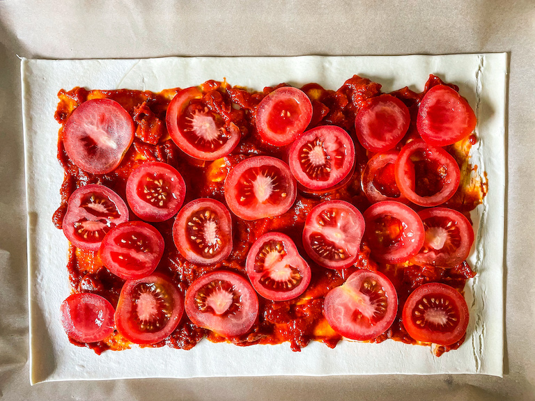 Sliced red tomatoes on top of tomato jam, on a sheet of puff pastry
