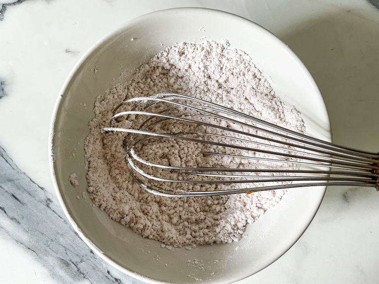 Dry ingredients in a white bowl with a wire whisk