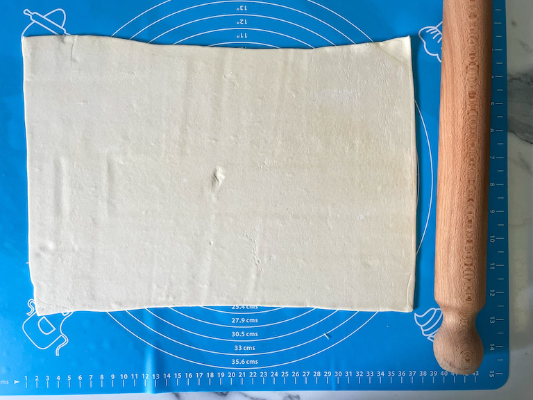 Puff pastry and a rolling pin on a blue rolling mat