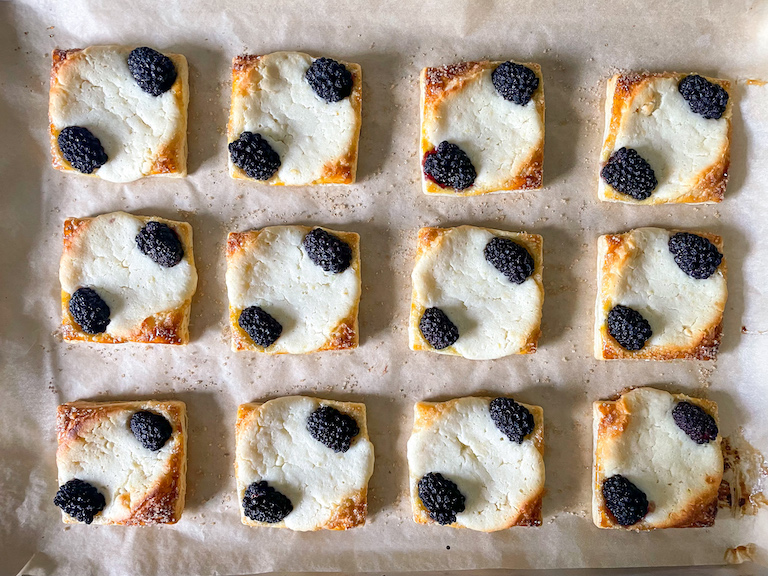 Squares of puff pastry with cheese filling and blackberries, on a parchment lined tray