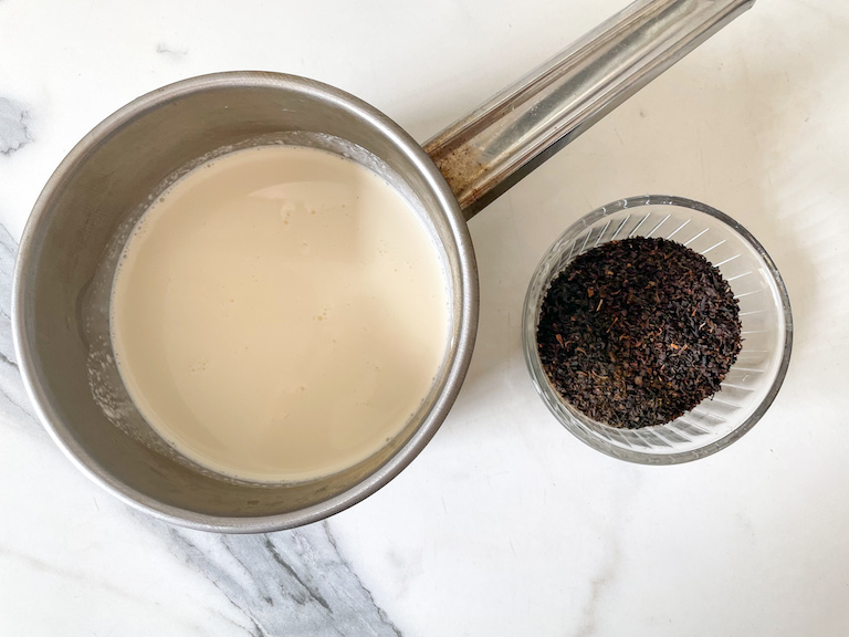 A saucepan of cream and a dish of loose leaf Earl Grey tea on a marble countertop