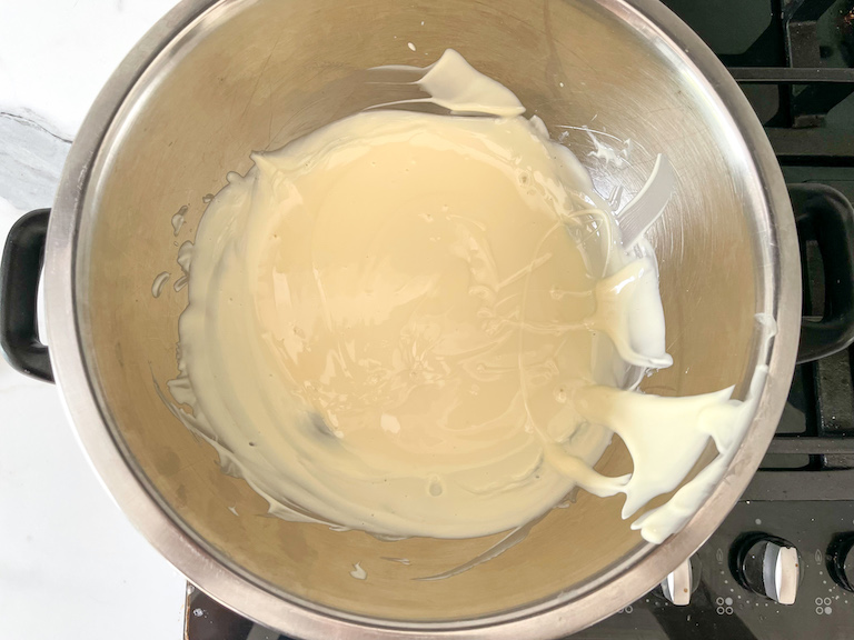 Melted white chocolate in a metal bowl on the stovetop
