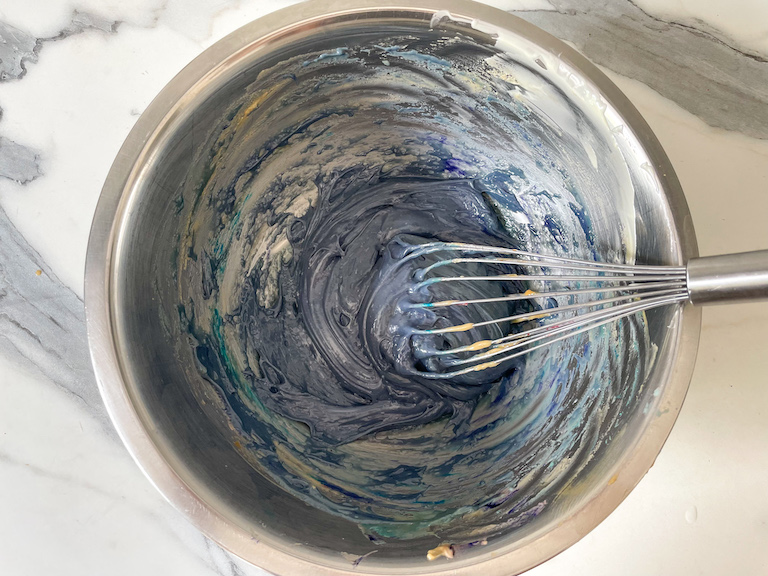 A bowl of ganache with blue food coloring added, and a whisk