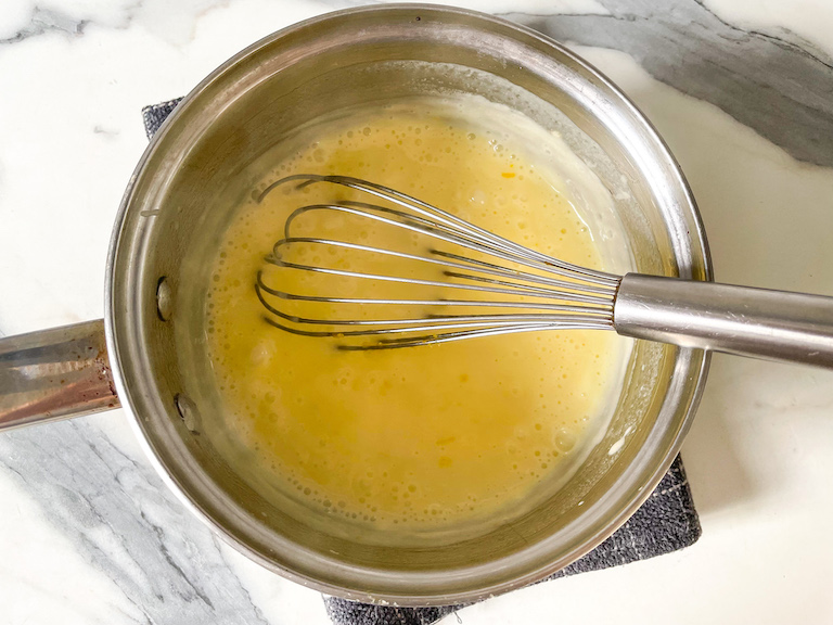Lemon posset mixture in a saucepan with whisk