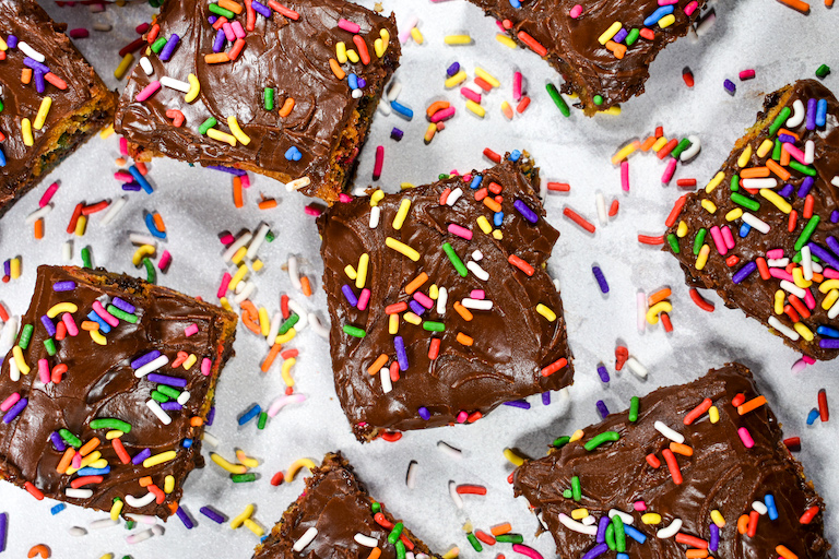 Chocolate chip cookie bars and rainbow sprinkles on a white surface