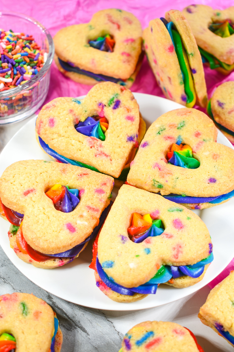 A plate of heart shaped buttercream rainbow cookies
