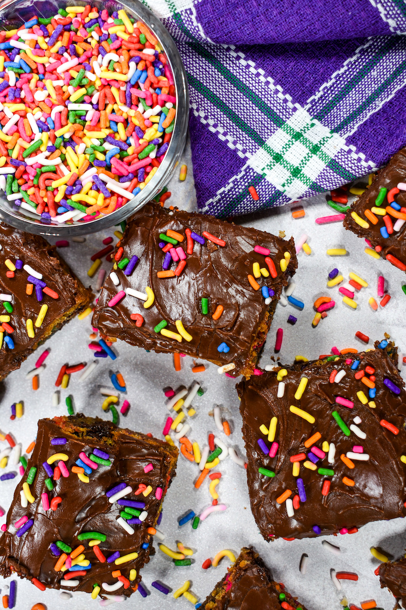 Frosted chocolate chip cookie bars, bowl of rainbow sprinkles, and purple plaid towel