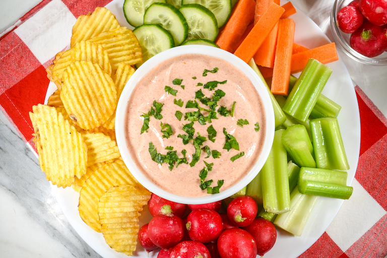 Greek yogurt sriracha sauce in a bowl, surrounded by chips and raw vegetables