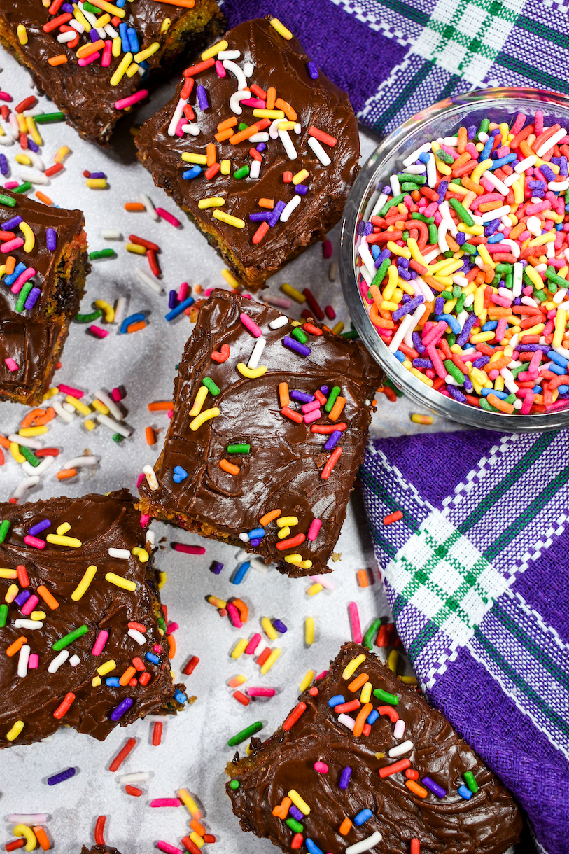 Purple tea towel and chocolate chip bars on a white surface with bowl of rainbow sprinkles