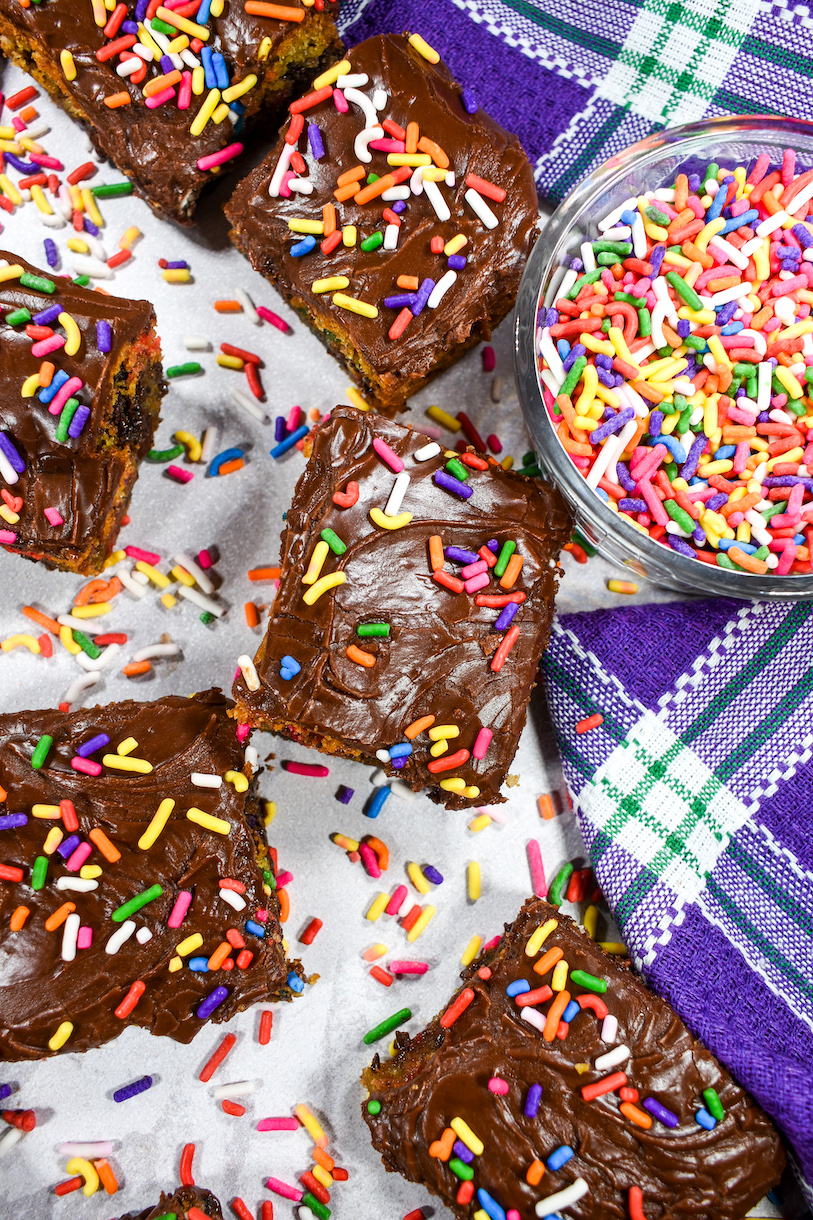 Purple tea towel, rainbow sprinkles, and chocolate chip cookie bars on a white surface