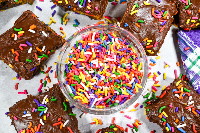 Bowl of rainbow sprinkles surrounded by chocolate chip bars
