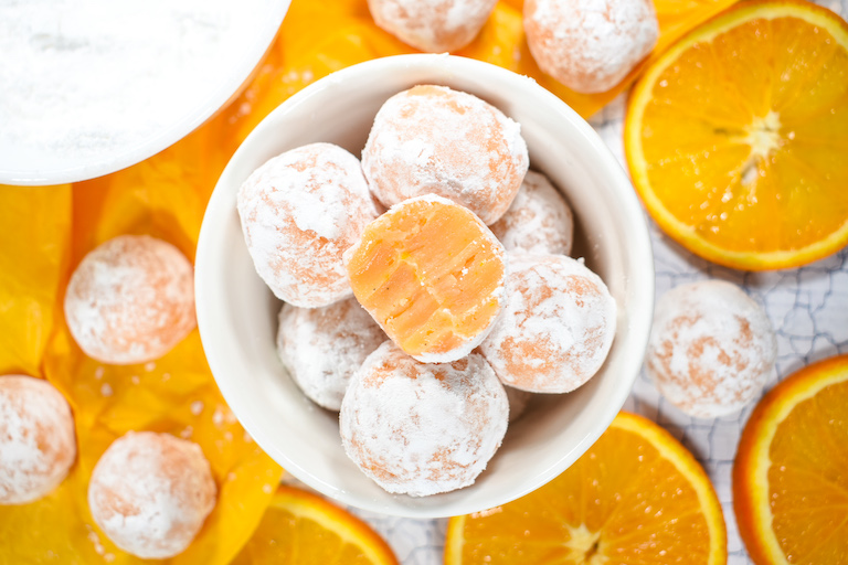 Looking down into a bowl of orange truffles, surrounded by sliced oranges