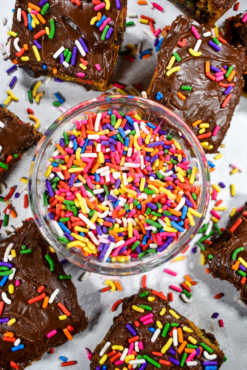 a dish of rainbow sprinkles surrounded by chocolate chip cookie bars