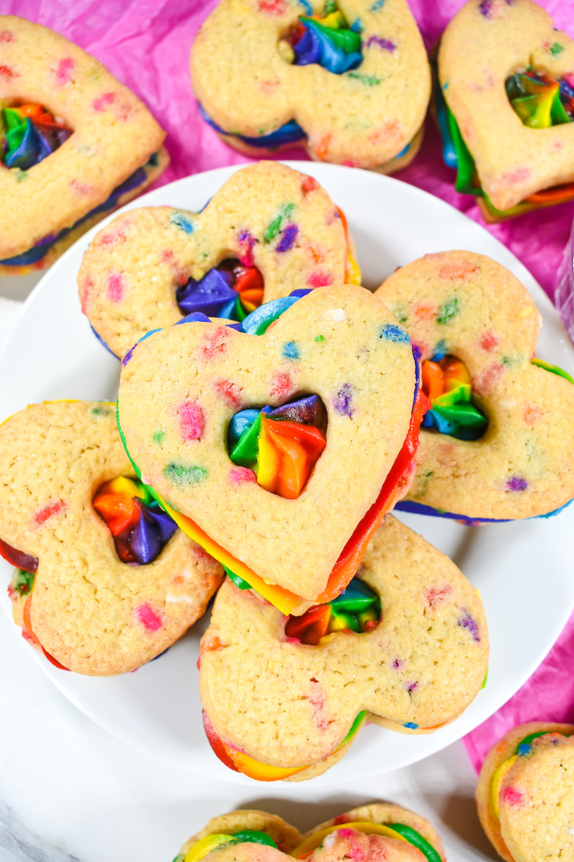 A plate of heart shaped buttercream rainbow cookies
