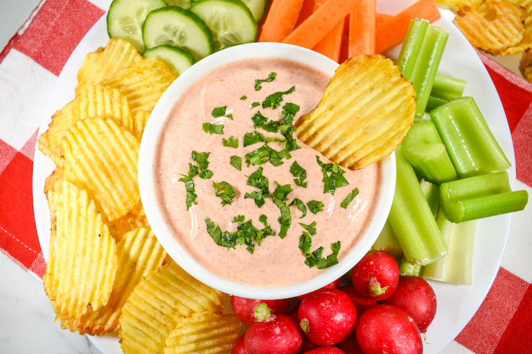 A bowl of sriracha dip with chips and raw vegetables