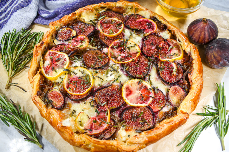 Horizontal shot of a fig and goat cheese tart with sprigs of rosemary and fresh figs