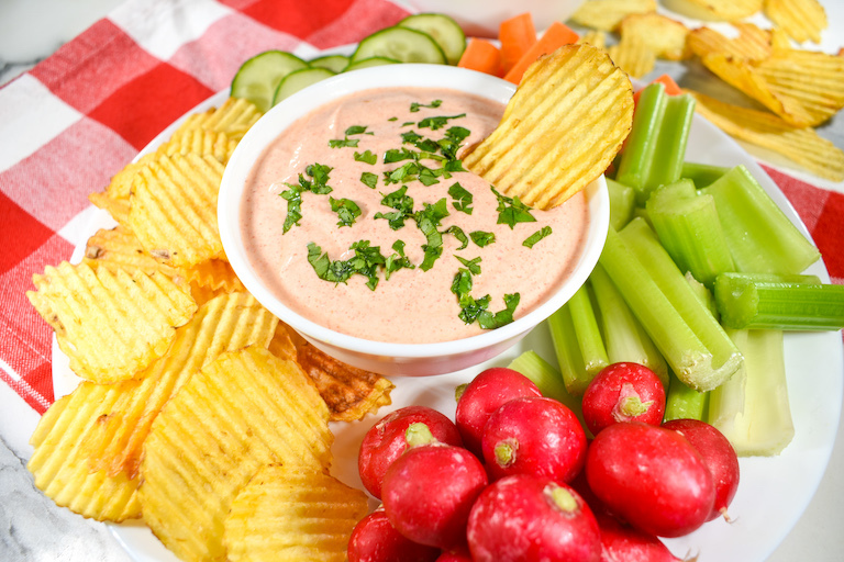 A bowl of homemade greek yogurt dip on a a plate, surrounded by chips and vegetables