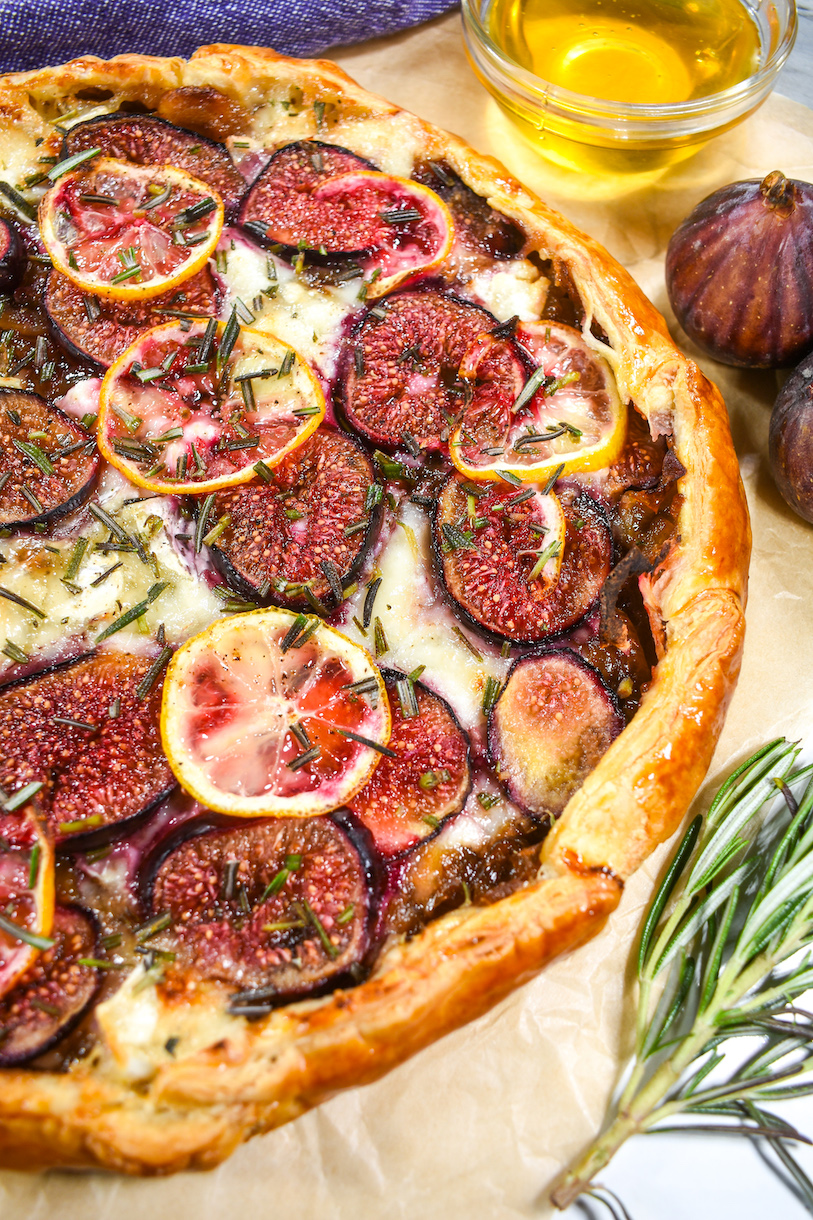 A puff pastry tart with goats cheese and figs, alongside fresh figs and a dish of honey