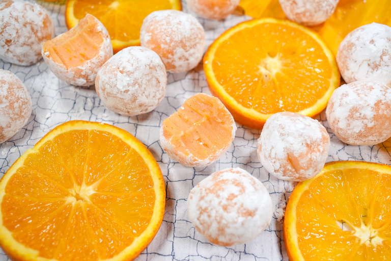 Orange truffles and sliced oranges on a white textured surface