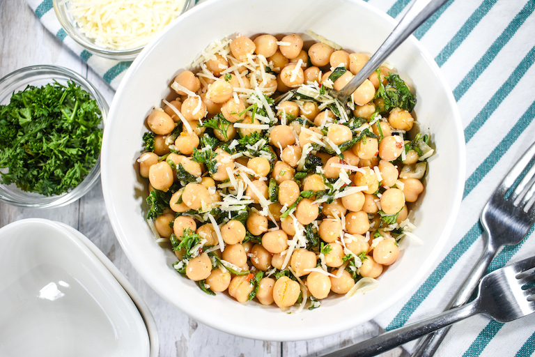 Dish of chickpea salad with small bowls of cheese and herbs