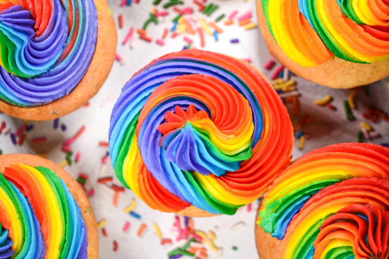 Rainbow cupcakes on a white surface with sprinkles