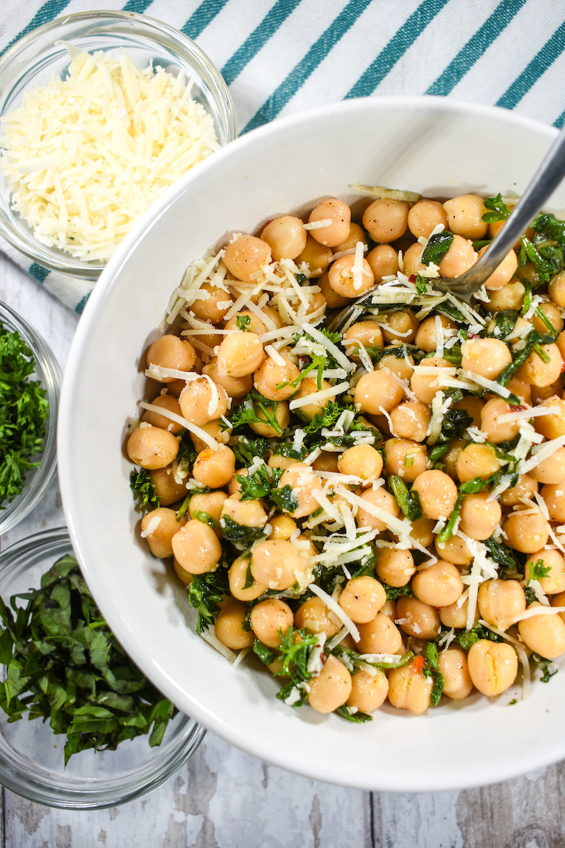Bowl of chickpea salad with small bowls of cheese and herbs and a striped towel